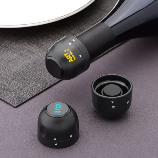 A drink bottle stopper in black, featuring a logo, designed for champagne. Includes two additional similar stoppers.