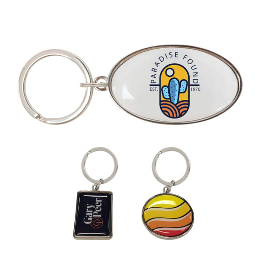 A custom-shaped metal keyring in silver, featuring an oval design with a colourful logo, alongside two smaller keyrings.