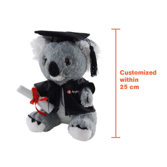 A plush koala wearing a graduation gown and cap, holding a scroll, grey with white accents and a logo on its robe.