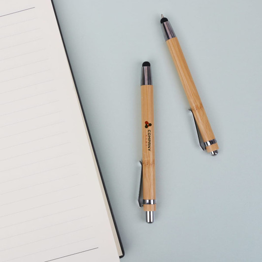 Bamboo pens with stylus nibs in a natural finish, placed beside a blank notebook. One pen features a branding logo.