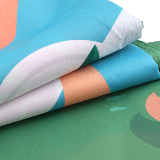 A folded outdoor blanket featuring a vibrant design with blue, green, and peach colours, along with a logo.