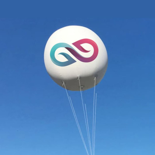 An inflatable advertising balloon in white, featuring a logo with teal and pink elements, floating against a blue sky.