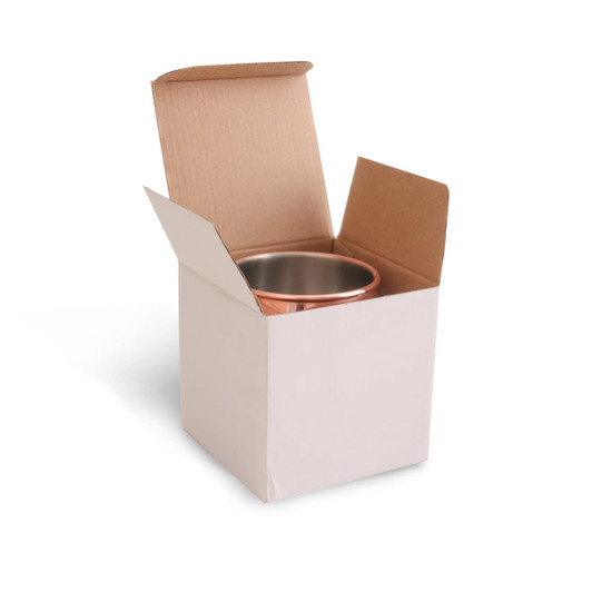 A copper Moscow Mule mug inside an open cardboard box. The mug has a shiny finish and features a logo.