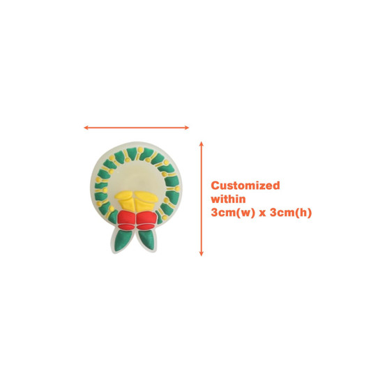 A circular shoe charm in yellow, green, and red, featuring a floral design, with a logo.