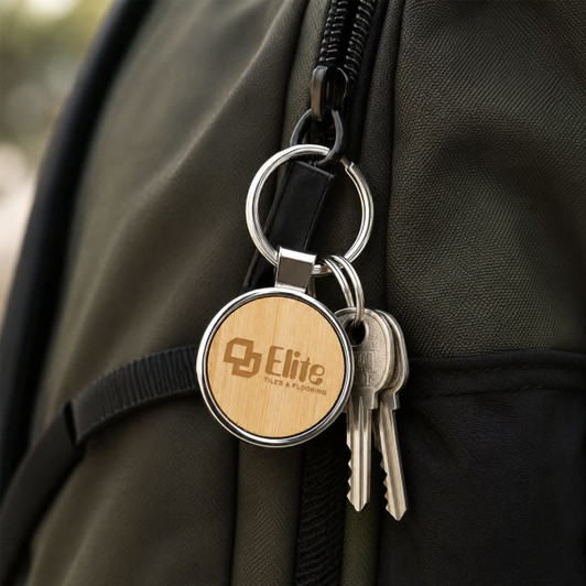 A round wooden keyring with a silver metal ring, attached to a dark green backpack alongside keys.