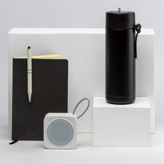 A black drink bottle, a black notebook, a white speaker, and a pen arranged on white pedestals. All products have branding.