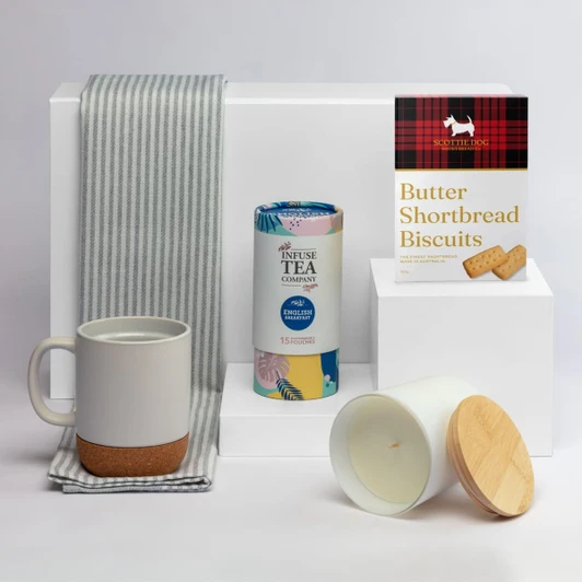 A coffee mug in grey and cork, a tea canister, a candle with a wooden lid, and shortbread biscuits, arranged on a white background.