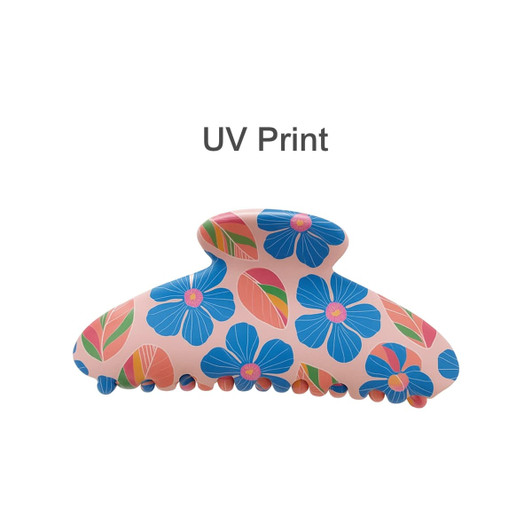 A floral hair clip featuring a pink background with blue flowers and colourful leaves, designed with UV print.