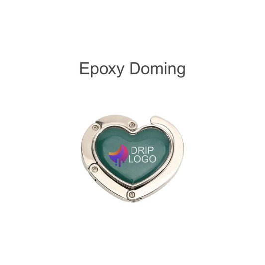 A heart-shaped, foldable desk hook in silver with a green epoxy finish and a logo.