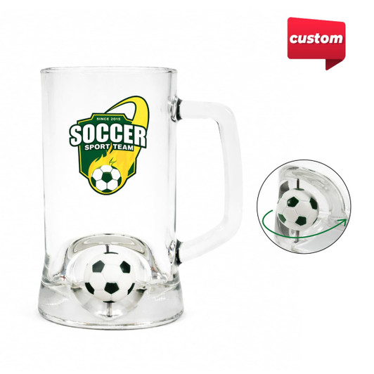 A clear beer glass featuring a soccer ball spinner toy inside and a logo. The glass has a sturdy handle.