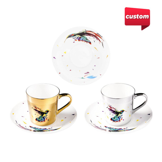 A set of two coffee mugs in gold and silver, featuring colourful bird designs, with matching saucers.