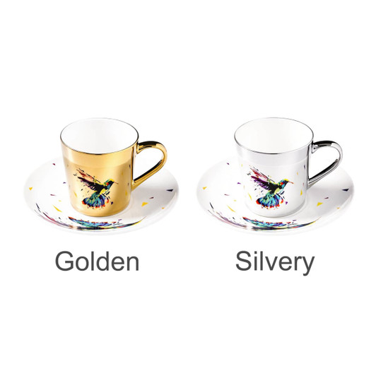 A coffee mug set featuring a golden and a silvery mug, each with a colourful bird design and matching saucers.