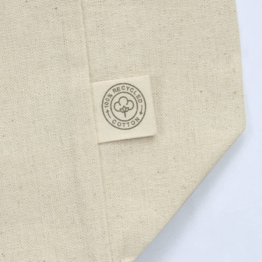A cream-coloured tote bag made from 100% recycled cotton, featuring a tag with a logo.