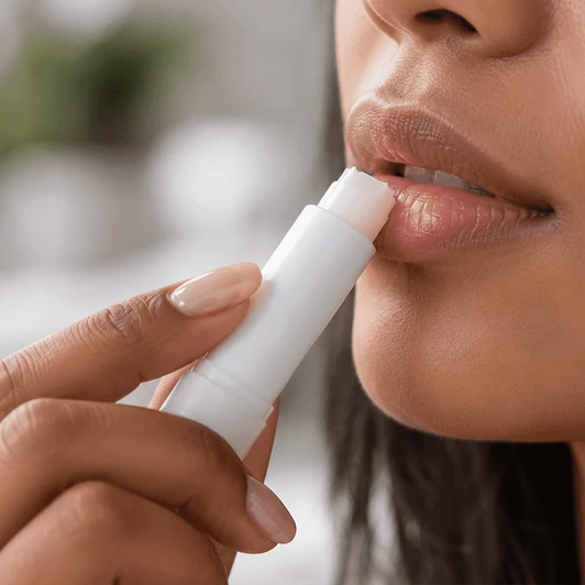 A twist lip balm in a white container being applied to lips. The person has light skin and natural-looking makeup.