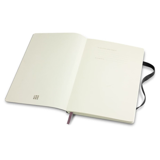 A large, soft-cover notebook in white with a black ribbon bookmark and an interior featuring blank pages. It has a logo.