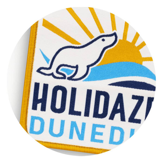 A woven patch featuring a yellow and blue design with a sun and a playful seal silhouette.