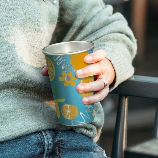 A drink cup in teal and yellow featuring colourful floral and citrus designs. It has a metallic interior and branding.