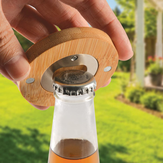 A drink bottle opener coaster made of bamboo, showcasing a person using it on a bottle in a garden setting.