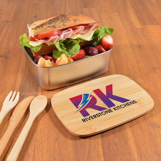 A stainless steel lunch box with a wooden lid and a colorful logo, filled with a sandwich and fresh fruit.