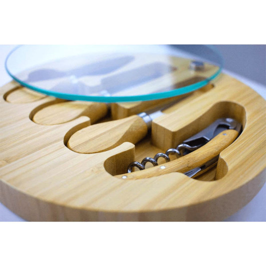 A round bamboo cheese board set with glass lid and wooden-handled cheese tools and a corkscrew.