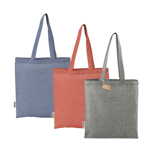 Three recycled cotton twill tote bags in blue, red, and grey, each featuring a handle and a logo label.