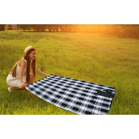 A large black and white checkered picnic rug laid out on grass, with a woman smiling while holding one side.