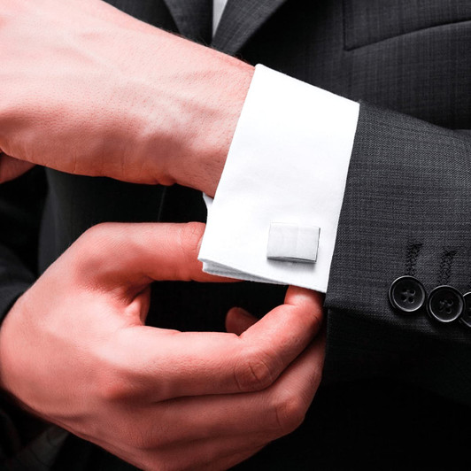 Silver plain cufflinks attached to a white dress shirt's cuff, worn with a black suit jacket.