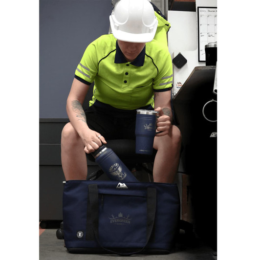 A blue drink bottle and mug sit next to a dark blue duffel bag, with a person in a high-visibility shirt and helmet.