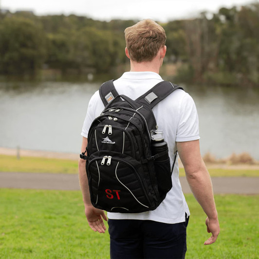 A black High Sierra Swerve 17" backpack with dual water bottle pockets is worn by a person standing outdoors near water.
