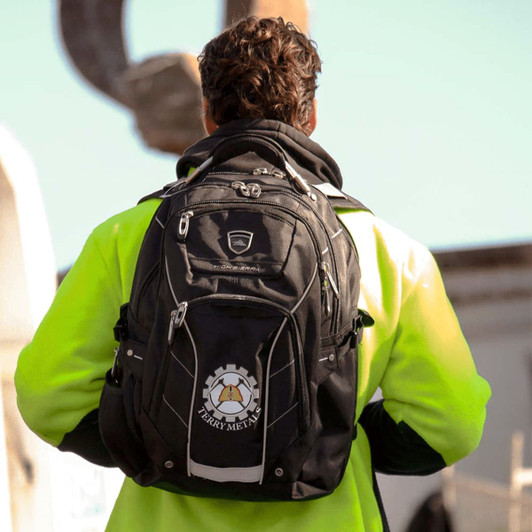 A black High Sierra Elite Fly-By 17" computer backpack with a logo, worn by a person in a high-visibility jacket.