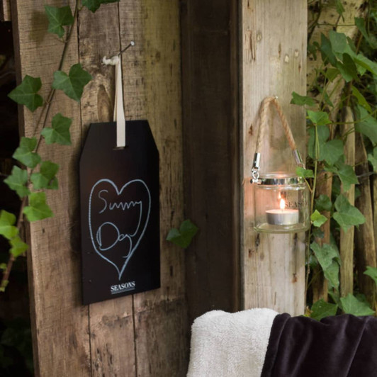 A blackboard shaped like a tag features a chalk drawing, displayed next to a glass lantern with a candle.