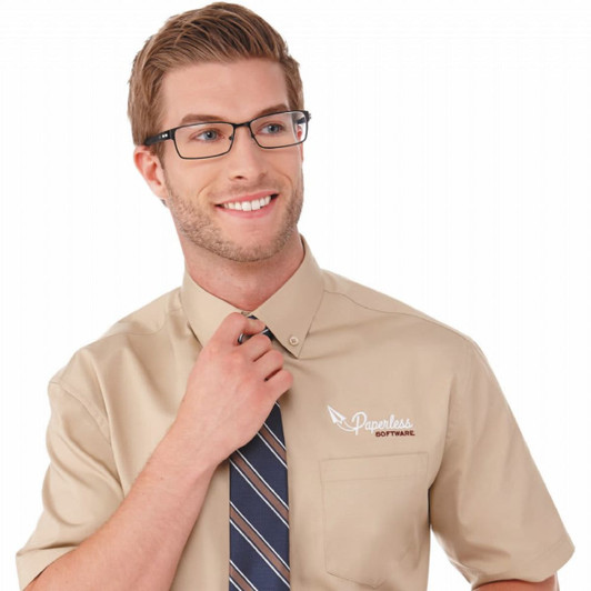 A short sleeve, beige button-up shirt with a logo on the left chest, worn by a man adjusting his tie.