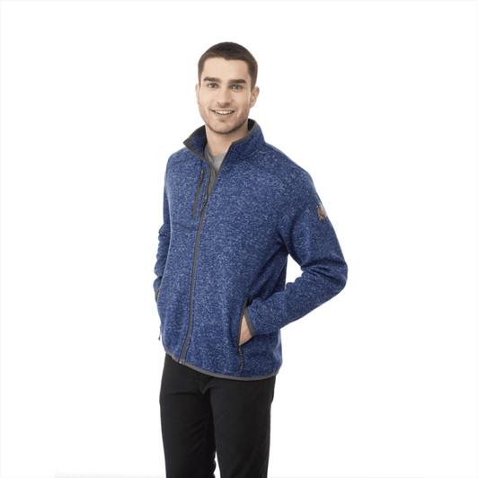 A man wearing a blue Tremblant Knit Jacket, featuring a zip front and standing with one hand in his pocket.