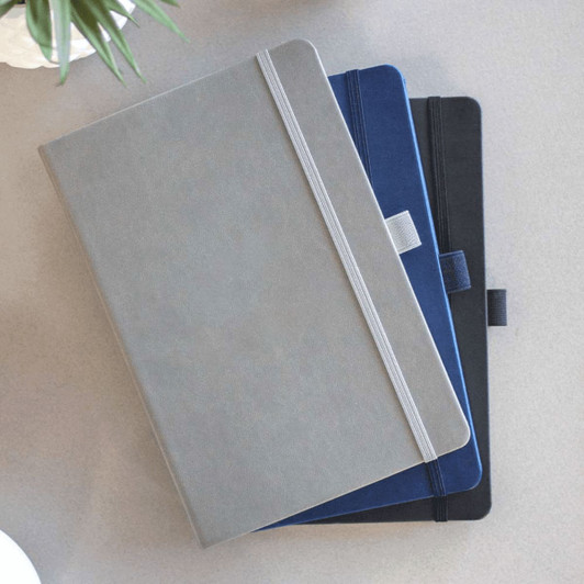 A set of three Mano Recycled Hard Bound JournalBooks in grey, navy, and black, featuring elastic closures and branding.