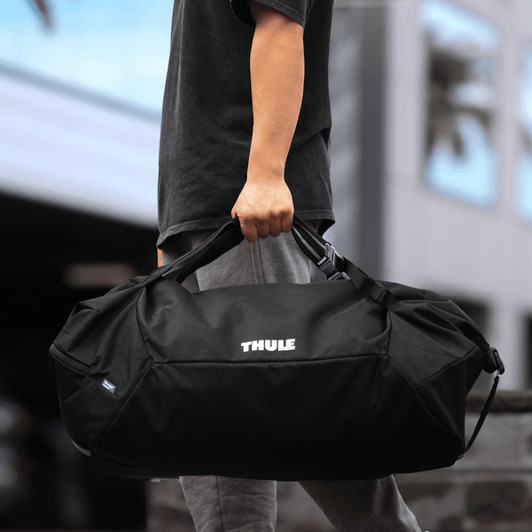 A black duffel bag with a mid blue accent and a logo, being held by a person.