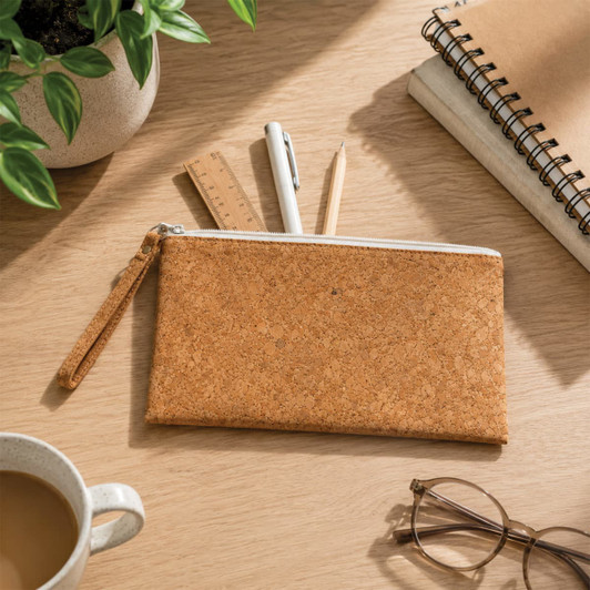 A cork pencil case with a zippered closure, surrounded by pens, a ruler, a notepad, and a cup of coffee.