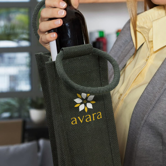 A drink bottle carrier in green jute with a decorative logo, held by a person in a grey blazer.