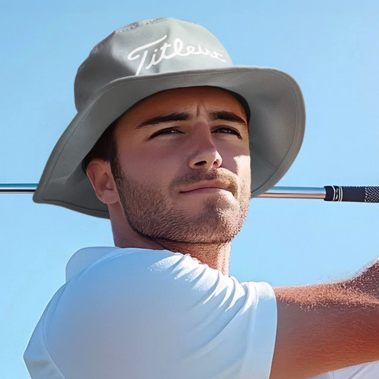 A grey bucket hat with a logo, worn by a man against a clear blue sky while holding a golf club.