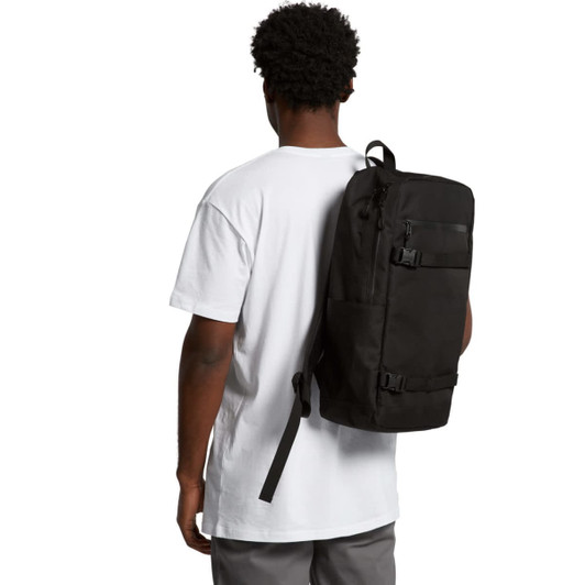 A man in a white t-shirt carries a black recycled strap backpack on his back, featuring multiple compartments and a logo.