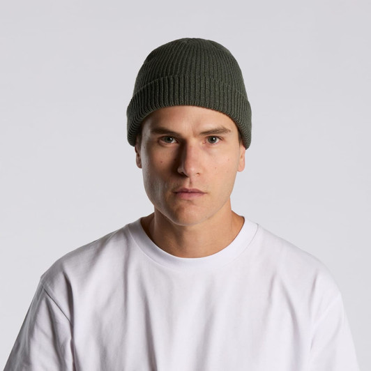 A green beanie worn by a person in a white t-shirt, featuring a subtle logo.