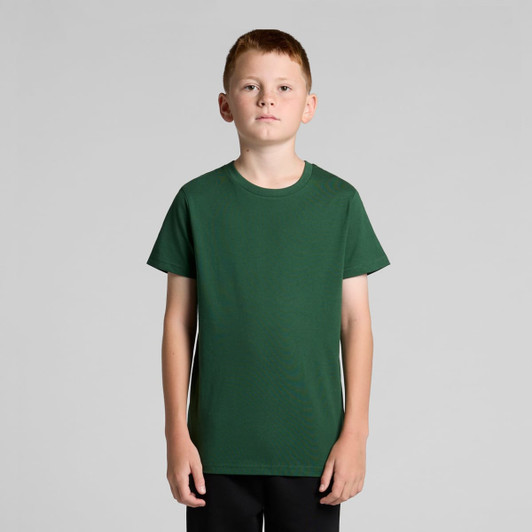 A young model is wearing a plain green youth staple tee, with short sleeves and a crew neck.