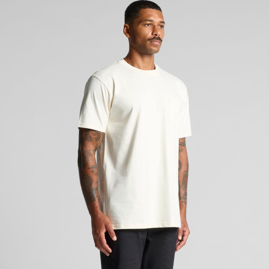 A plain cream Classic Pocket Tee featuring a front pocket and short sleeves, modelled by a person with tattoos.