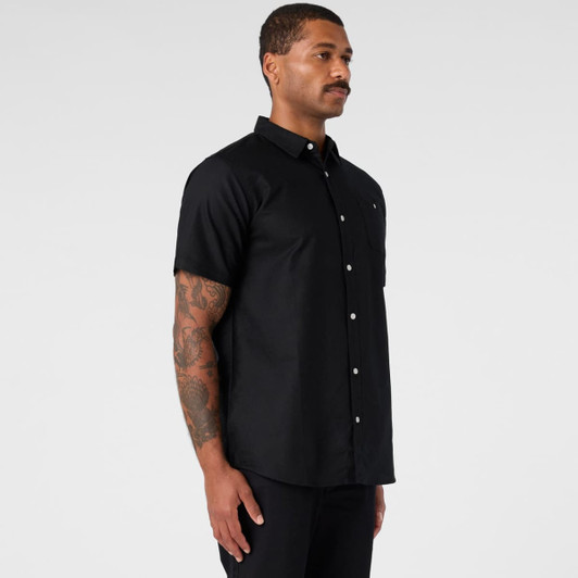 A black short-sleeve button-up shirt displayed on a model standing sideways, featuring a logo on the chest.