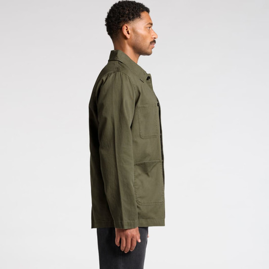 A man wearing an olive green canvas chore jacket, viewed from the side, with a simple design and a logo present.