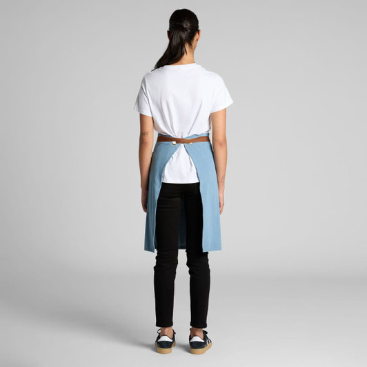 A denim half apron in blue, worn over black pants, with a brown belt detail at the back.