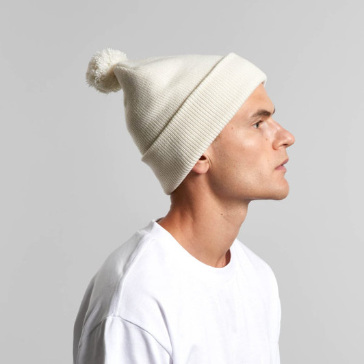 A white Pom Pom Beanie displayed on a model, featuring a fluffy pom pom on top and ribbed detailing.