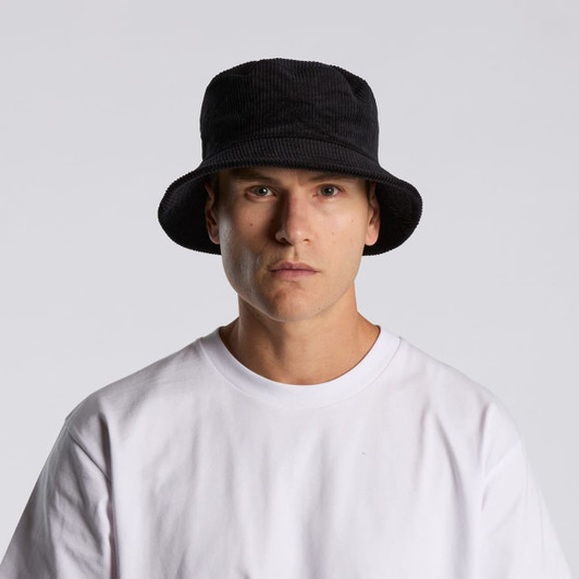 A black cord bucket hat worn by a model, paired with a plain white t-shirt. The hat features a branding logo.
