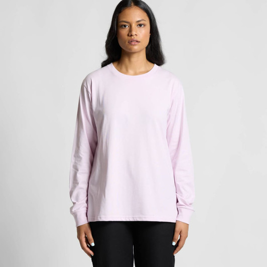 A long-sleeve T-shirt in light pink, featuring a simple design and a logo on the front. Model wears black pants.