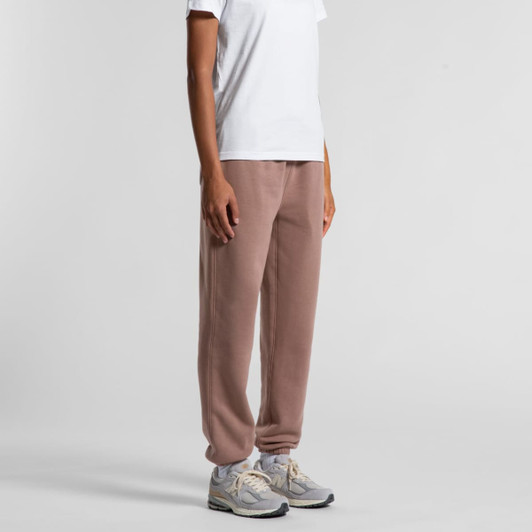 Track pants in a soft brown hue, featuring a relaxed fit and tapered cuffs, worn with a white t-shirt and grey sneakers.