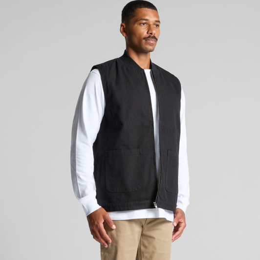 A black canvas heavy vest worn over a white long-sleeve shirt, featuring two front pockets and a zip closure.